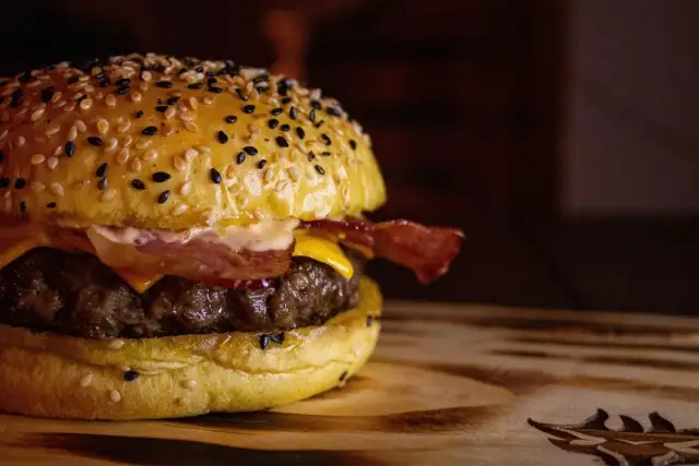 Apetyczny burger z sezamową bułką, serem, bekonem i soczystym mięsem na drewnianej desce.