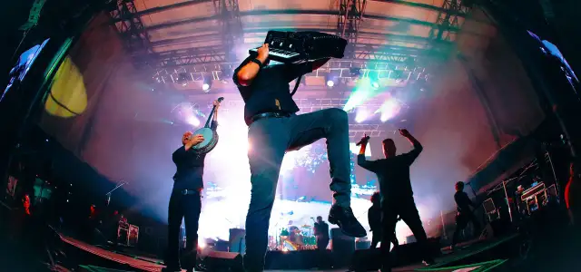 Energetyczne koncerty Dropkick Murphys: muzyk gra na akordeonie, inny na banjo, a w tle wokalista z mikrofonem.