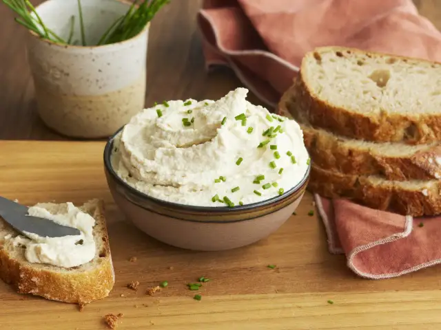 Cremiger veganer Frischkäse, garniert mit Schnittlauch, wird auf Brot gestrichen. Perfekt, um veganen Frischkäse selber machen zu lernen.