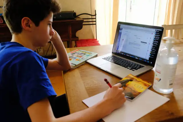 Chłopiec uczy się zdalnie, przed nim laptop, podręczniki i notatnik. Mam nadzieję, że jego **oceny** będą dobre.