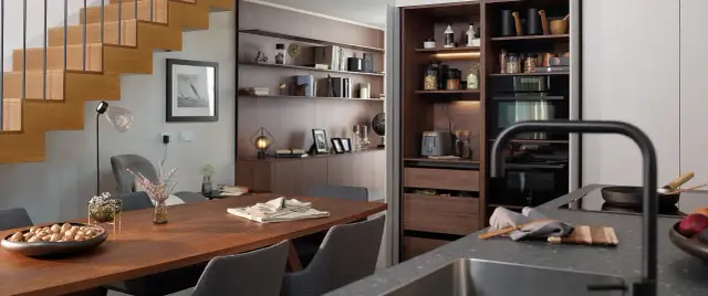 Comedor y zona desayuno cocina con mesa de madera, sillas grises y estanterías empotradas.