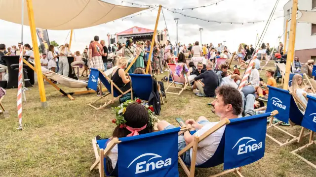 Ludzie odpoczywają na leżakach z logo Enea podczas festiwalu. W tle scena i tłum.