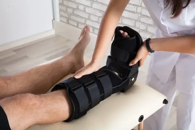 Fizjoterapeuta zakłada pacjentowi stabilizator na nogę, pokazując różne rodzaje gipsu medycznego.