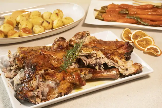 Pierna de cordero lechal al horno jugosa, dorada y tierna, acompañada de patatas asadas y zanahorias glaseadas.