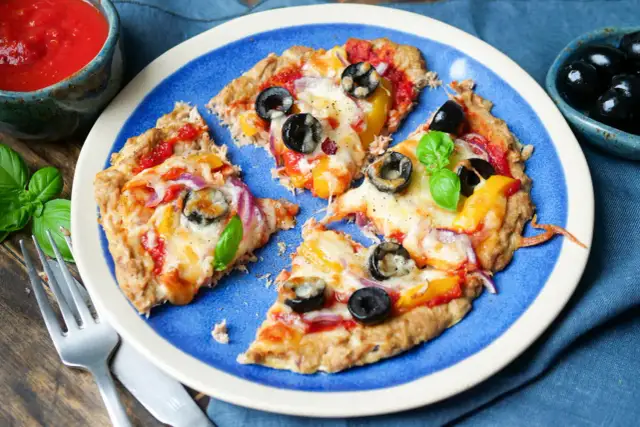 Low carb pizza thunfisch mit Oliven und Paprika auf blauem Teller, daneben eine Schale mit Tomatensauce und frischem Basilikum.