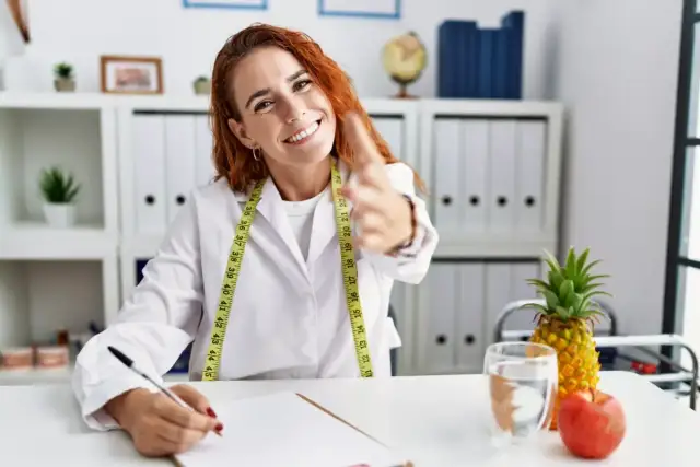 Dietetyczka z miarką, pisząca przy biurku, z ananasem i jabłkiem.