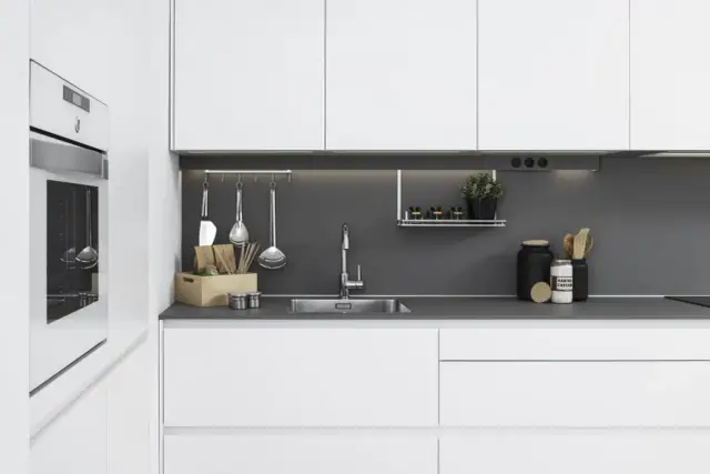 Moderna cocina blanca y gris con electrodomésticos integrados, fregadero de acero inoxidable y utensilios de cocina colgados.