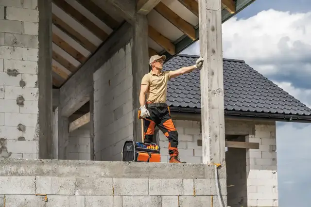 Budowlaniec sprawdza fundament pod domek 35m2. W tle widać dach i ściany z bloczków.