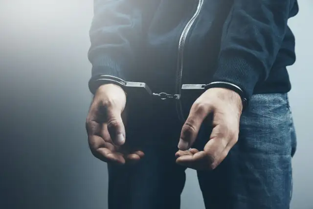 Dłonie osoby w kajdankach, ubranej w bluzę i jeansy.