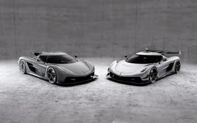 Dwa lśniące Koenigsegg Jesko, jeden szary, drugi srebrny, stoją obok siebie na betonowym tle.