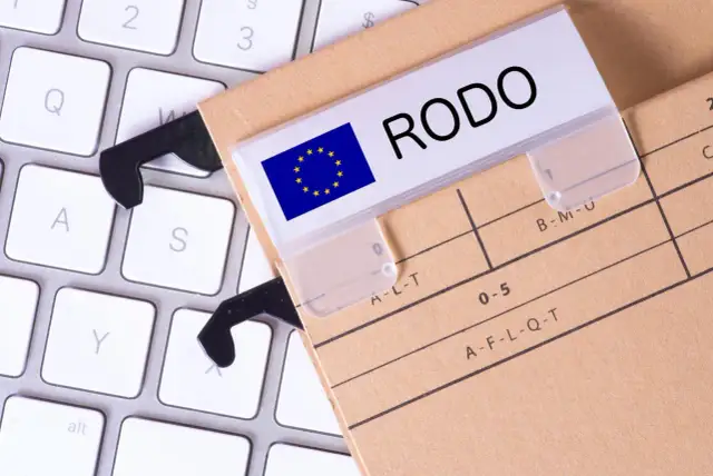 Dokumentacja RODO na teczce z etykietą "RODO" i flagą UE, leżąca na klawiaturze. To rejestr czynności przetwarzania.