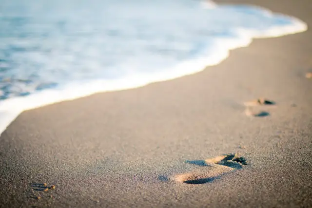 Ślady stóp na piaszczystej plaży, gdzie fale obmywają brzeg. Choć w Polsce jest tylko jedno morze, Bałtyk, to jego piękno jest niezmierzalne.