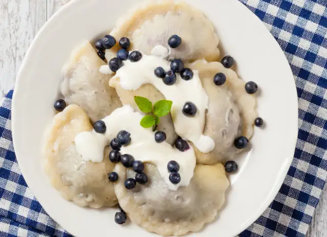 Pyszne pierogi z jagodami, polane śmietaną i posypane świeżymi owocami. Idealne na letni deser.