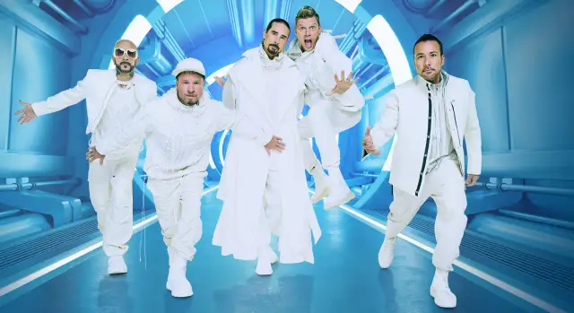 Backstreet Boys w białych strojach, gotowi na koncert. Ich energia jest zaraźliwa, a futurystyczna scenografia podkreśla ich styl.