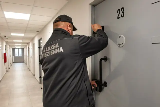 Strażnik więzienny przy drzwiach celi nr 23. Czy pobyt w zakładzie karnym wlicza się do emerytury? To pytanie nurtuje wielu.