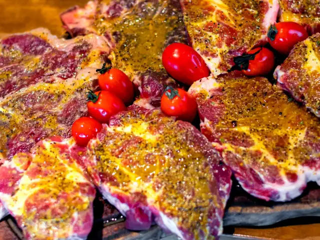Soczyste plastry karkówki, marynowane i przyprawione, gotowe do grillowania. Obok leżą czerwone pomidorki koktajlowe.