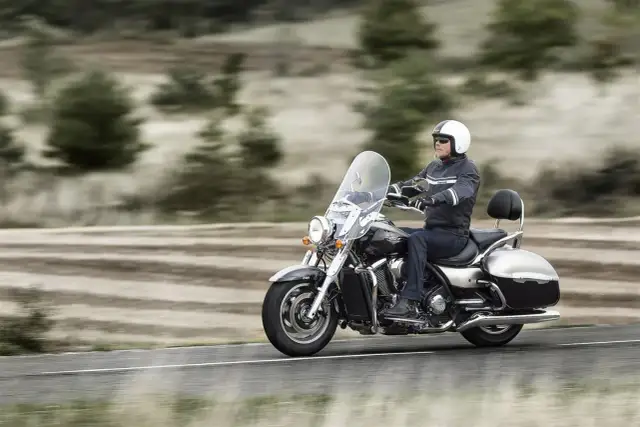 Mężczyzna w kasku jedzie na dużym motocyklu, który można nazwać chopperem. W tle rozmyty krajobraz.