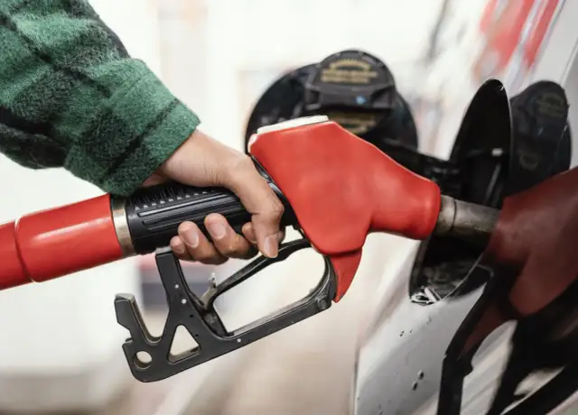 Dłoń w zielonej koszuli trzyma czerwoną dyszę dystrybutora paliwa. Czy to diesel to ropa czy benzyna? Tankowanie samochodu.