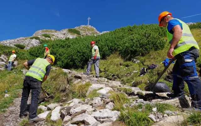 Pracownicy konserwują szlak na Giewont. Czy szlak na Giewont jest trudny? Widać krzyż na szczycie, a teren jest kamienisty.