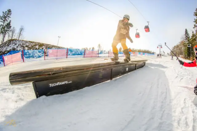 Snowboardzista na grindboxie w **Jaworzynie Krynickiej snowparku**. W tle kolejka linowa i inni narciarze.
