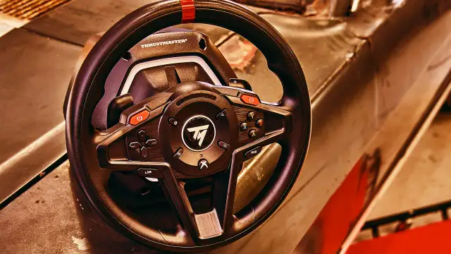 Kierownica Thrustmaster z przyciskami, na tle metalowej powierzchni.