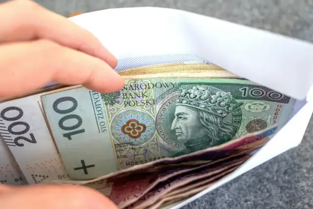 Dłoń wsuwa kopertę z banknotami 100 i 200 zł. Zastanawiasz się, renta wdowia komu przysługuje?