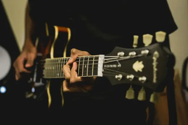 Dłoń grająca akord na gryfie gitary elektrycznej.