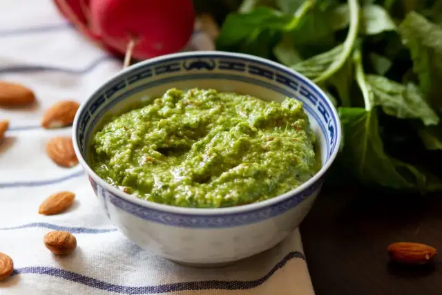 Pesto z liści rzodkiewki, z migdałami i świeżymi ziołami, w miseczce z niebieskim wzorem.