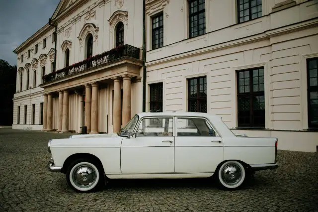 Biały Peugeot 404 na brukowanym dziedzińcu przed pałacem.