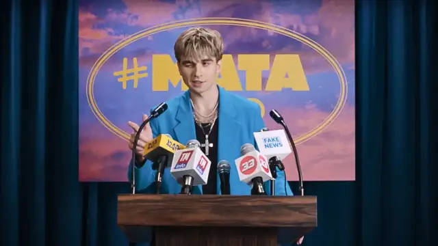 Mata w niebieskiej marynarce przemawia za mównicą z mikrofonami, na tle napisu "#MATA".