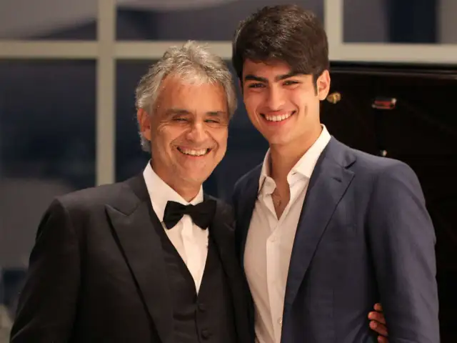 Andrea Bocelli z synem Matteo. Uśmiechnięci panowie w eleganckich strojach, młody Bocelli w granatowej marynarce.