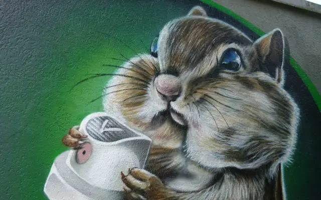 Graffiti eines Eichhörnchens, das eine Spraydose hält, vor grünem Hintergrund.