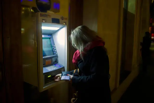 Kobieta przy bankomacie, wyciąga kartę. To symboliczny obraz mnożnika kreacji pieniądza w obiegu.