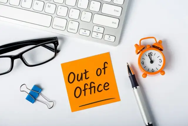 Biurko z klawiaturą, okularami, karteczką "Out of Office", zegarkiem i długopisem.