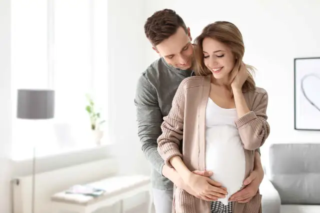 Szczęśliwy mąż obejmuje żonę w ciąży, okazując troskę i miłość. To piękny obraz wsparcia i oczekiwania na dziecko, symbolizujący opiekę na żonę po porodzie.