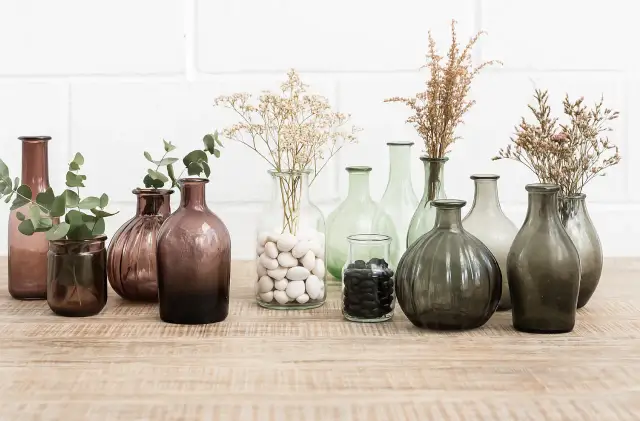 Variedad de jarrones de cristal grandes, algunos con ramas secas y hojas verdes, perfectos para decorar.