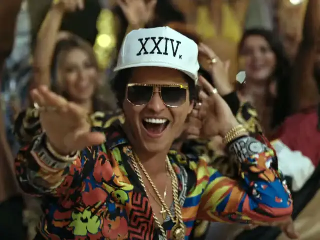 Bruno Mars w Polsce! Wesoły artysta w kolorowej koszuli i czapce z napisem "XXIV K" tańczy wśród rozbawionych ludzi.