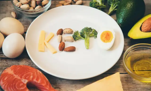 Czy dieta keto jest zdrowa? Na talerzu litery KETO z sera, orzechów, brokuła i jajka. Wokół łosoś, awokado, oliwa.