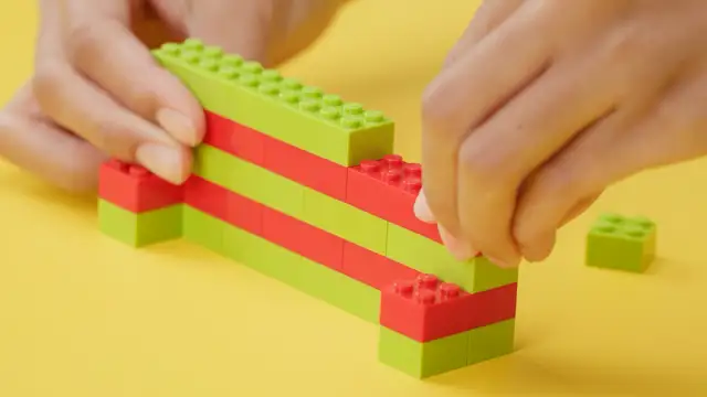 Dziecko buduje z zielonych i czerwonych klocków, pokazując, jak zbudować z klocków lego.