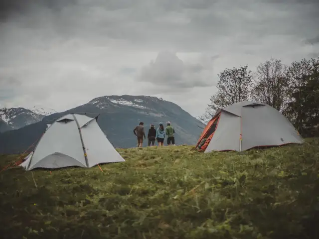 Dwa namioty na trawiastym zboczu górskim, z ludźmi stojącymi w tle.
