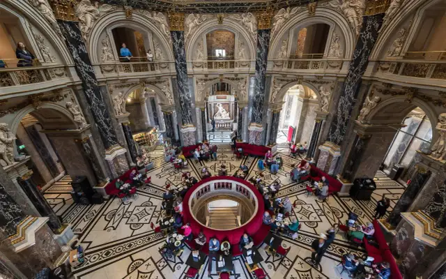 Wnętrze muzeum historii sztuki w Wiedniu z ludźmi przy stolikach i rzeźbą w centrum.