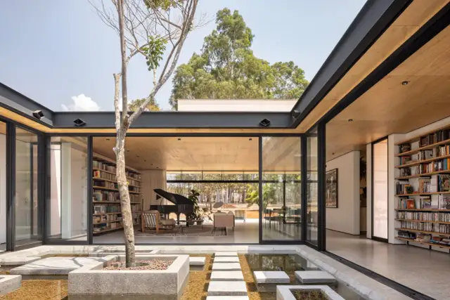 Modernas casas con patio interior central, un árbol solitario y un estanque de agua reflejan la luz natural.