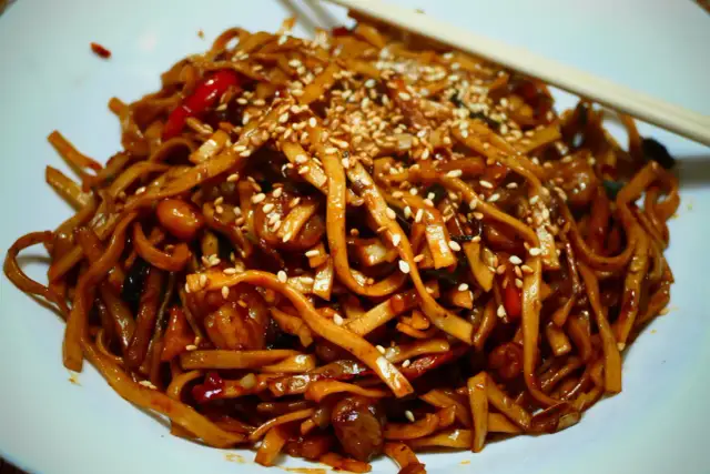 Makaron chow mein z sezamem i papryką na białym talerzu, z pałeczkami.