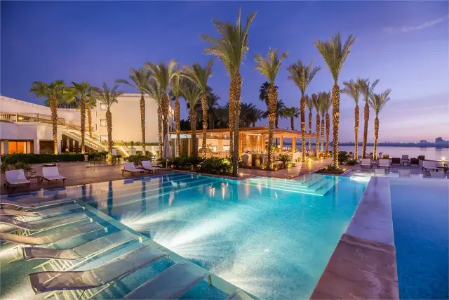 Luxury resort pool with palm trees and lounge chairs at dusk.