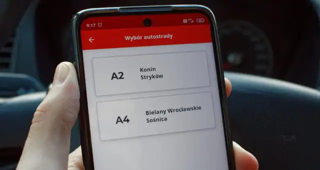 Dłoń trzyma smartfon z aplikacją do wyboru autostrady A2 Konin-Stryków i A4 Bielany Wrocławskie-Sośnica.