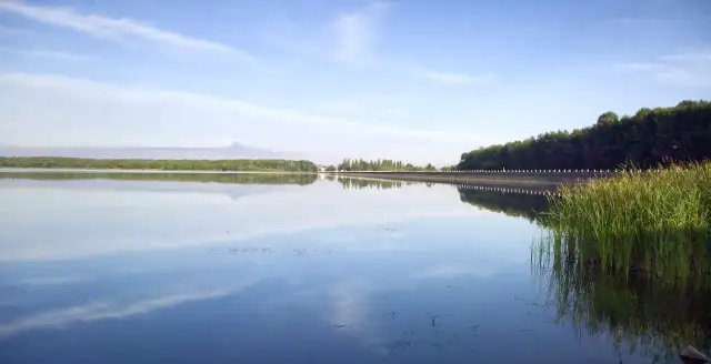 Spokojny zalew Dziećkowice z odbijającymi się w tafli wody chmurami i zielonym lasem w tle.