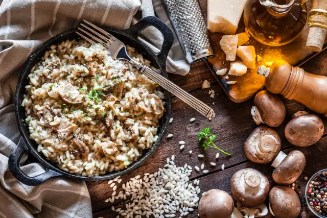 Un cremoso risotto de setas servido en sartén de hierro fundido, con champiñones frescos, arroz, queso parmesano y perejil picado.