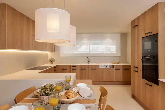 Cocina moderna con gabinetes de madera clara, encimeras blancas y una isla. Perfecta para tus ideas de cocinas.