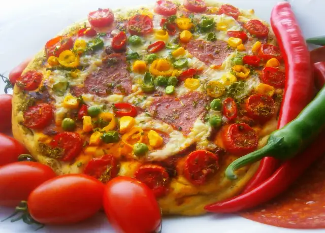 Pyszna pizza pepperoni z pomidorkami, papryką i zielonym groszkiem, otoczona świeżymi papryczkami chili i pomidorami.