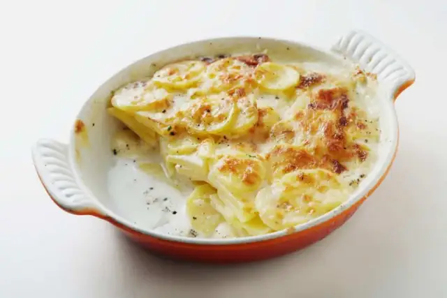 Patatas gratinadas con queso cremoso y dorado, recién salidas del horno en una cazuela naranja.